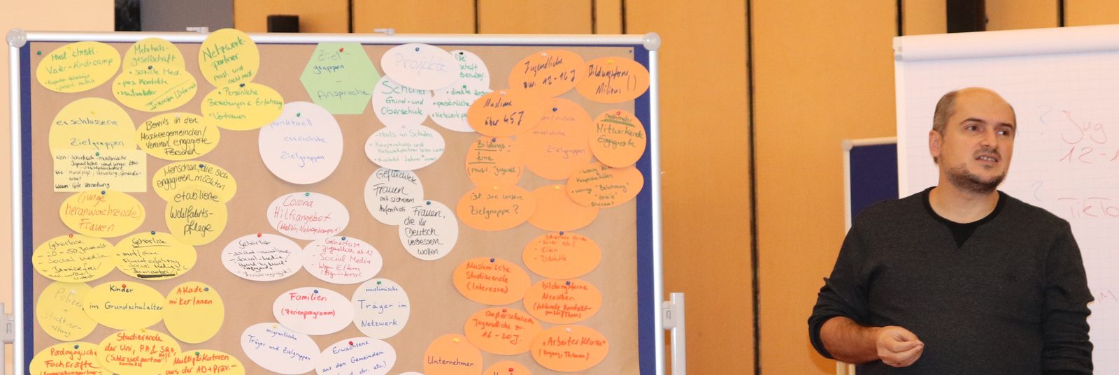 Engin Karahan steht in einem Seminarraum neben einer Moderationswand voller Karten