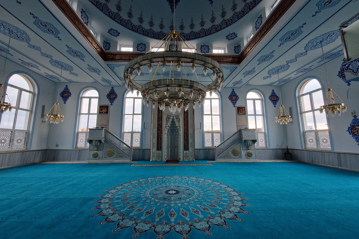 Leerer Gebetsraum einer Moschee mit blauem Teppich und Kronleuchter