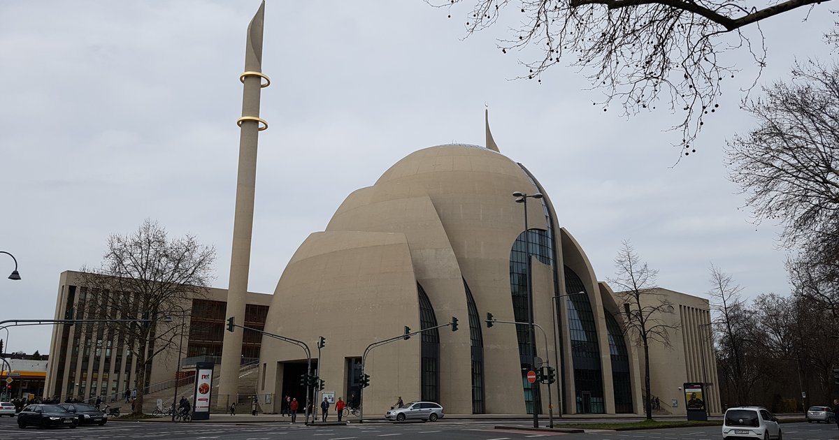 Außenansicht der DITIB-Zentralmoschee in Köln-Ehrenfeld mit Kuppel und Minarett, davor eine Straßenkreuzung mit Ampeln und kahlen Bäumen.