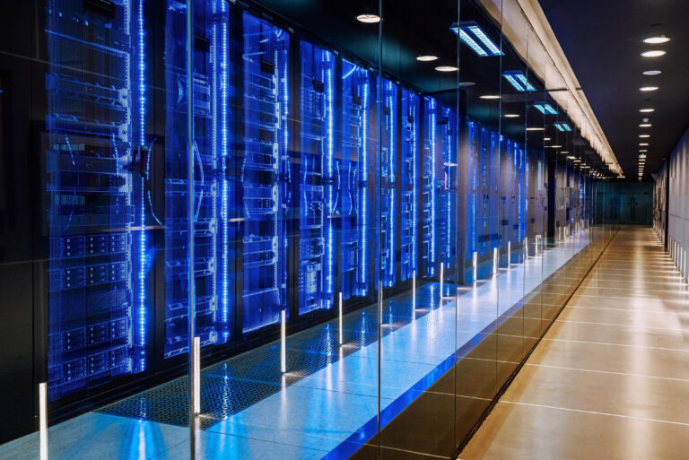 Blick in ein modernes Rechenzentrum mit blau beleuchteten Serverracks hinter Glas.